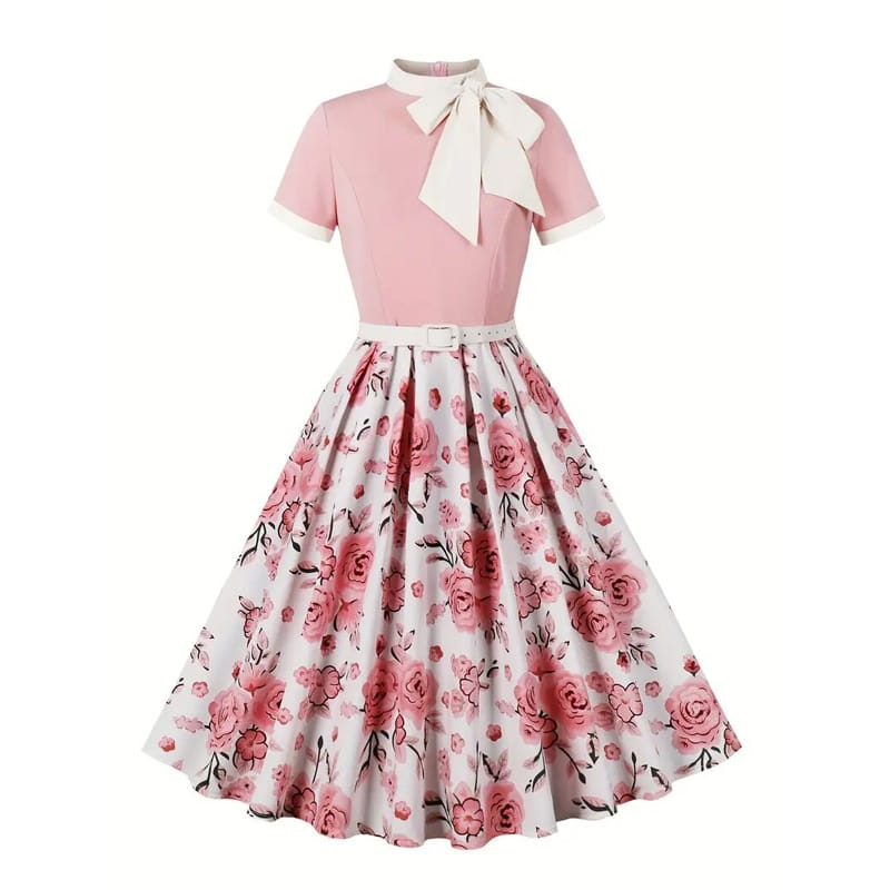 Screenshot of a real dress. A vintage-style dress with a pink fitted top, short sleeves, a large white bow at the neck, and a white flared skirt featuring a pink rose floral pattern. The dress has a matching white belt at the waist.