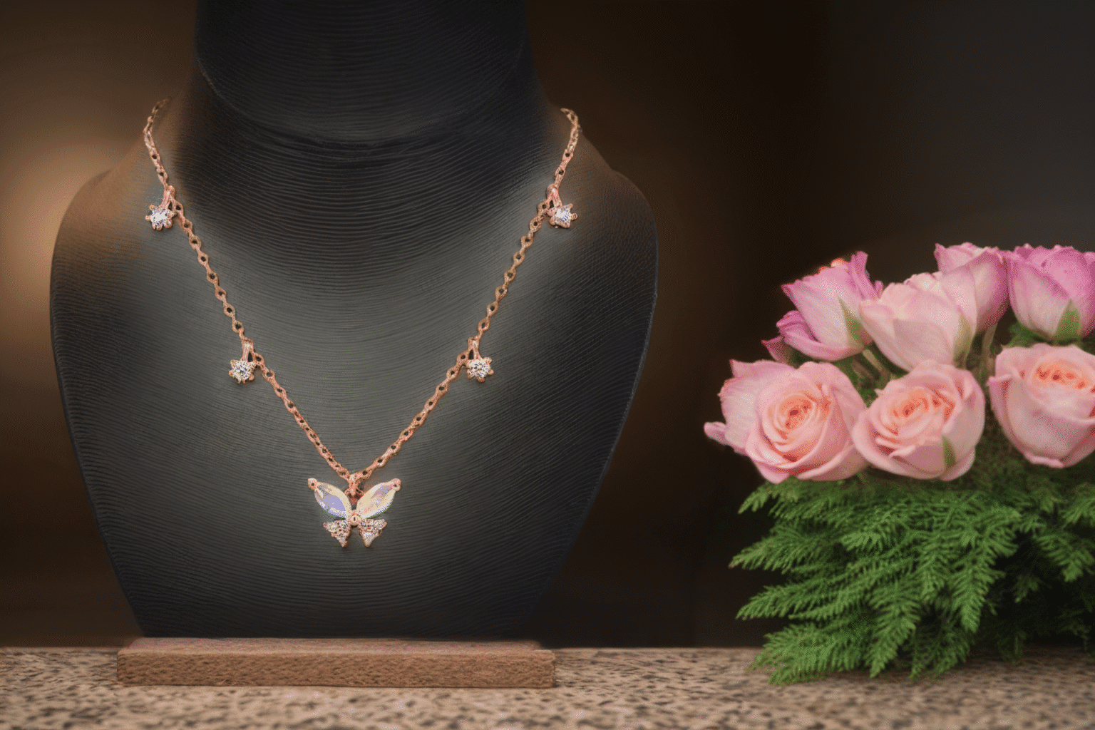 A gold butterfly necklace with matching earrings is displayed on a black stand next to a bouquet of pink roses and green ferns, set against a softly blurred brown background.